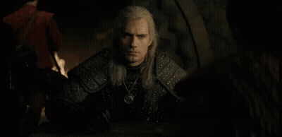 A Man With Long White Hair Is Sitting At A Table With A Necklace Around His Neck GIF