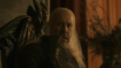 A Man With Long White Hair Is Sitting In A Chair With The Word Wine Below Him GIF