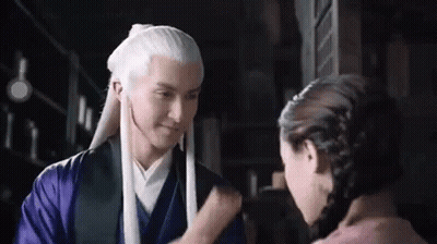A Man With Long White Hair Is Standing Next To A Woman In A Purple Dress . GIF