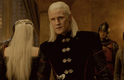 A Man With Long White Hair Is Standing Next To A Woman GIF