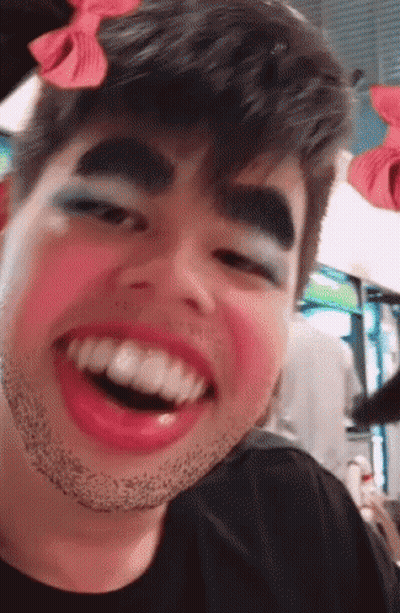 A Man With Makeup On His Face And A Bow On His Head Is Smiling GIF