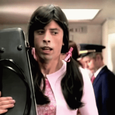 A Man With Pigtails Is Holding A Suitcase In A Hallway GIF