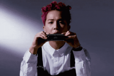 A Man With Pink Hair Is Holding A Black Object In Front Of His Mouth GIF