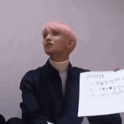 A Man With Pink Hair Is Holding A Piece Of Paper That Says Joshua . GIF