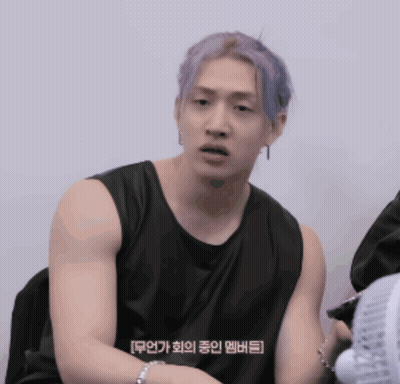 A Man With Purple Hair Is Wearing A Black Tank Top And Sitting Next To A Fan GIF