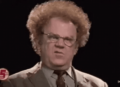 A Man With Red Curly Hair And Glasses Is Wearing A Suit And Tie And Making A Funny Face . GIF