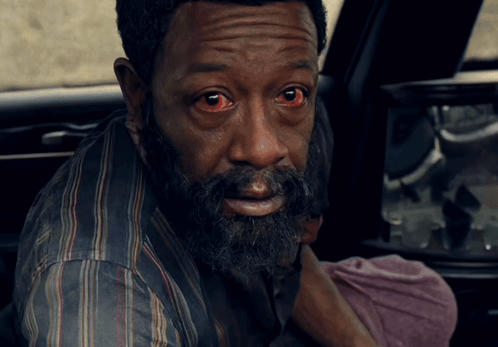 A Man With Red Eyes And A Beard Looks At The Camera GIF