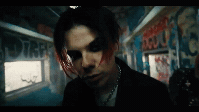 A Man With Red Hair And Black Makeup Is Standing In A Room With Graffiti On The Wall . GIF