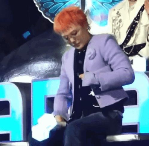 A Man With Red Hair Is Wearing A Purple Jacket And Holding A Microphone . GIF