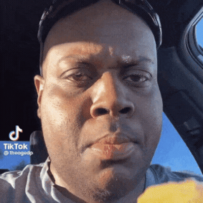 A Man With Red Lipstick On His Lips Is Sitting In A Car Eating A Piece Of Food . GIF
