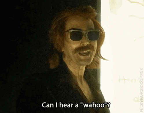 A Man With Sunglasses And A Mustache Is Standing In Front Of A Window And Talking . GIF
