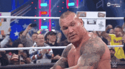 A Man With Tattoos Is Standing In A Wrestling Ring With A Crowd Watching . GIF