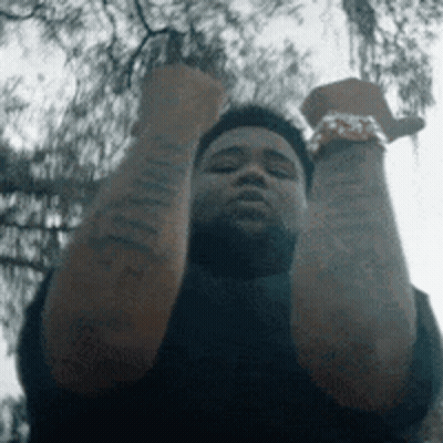 A Man With Tattoos On His Arms Is Holding His Fist Up In The Air . GIF