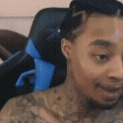 A Man With Tattoos On His Chest Is Sitting In A Chair . GIF
