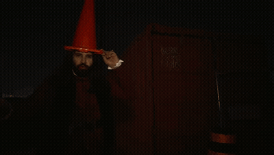 A Man With Vampire Teeth Wearing An Orange Cone Hat GIF