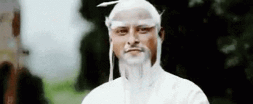 A Man With White Hair And A Beard Is Standing In Front Of A Tree And Looking At The Camera . GIF