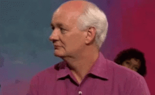 A Man With White Hair Is Wearing A Purple Shirt And Looking To The Side . GIF