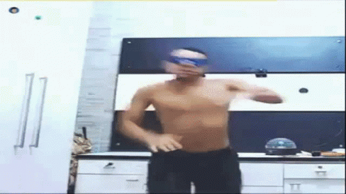 A Man Without A Shirt Is Dancing In A Kitchen Wearing Goggles . GIF