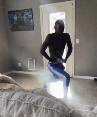 A Man Without A Shirt Is Dancing In A Living Room With A Couch . GIF