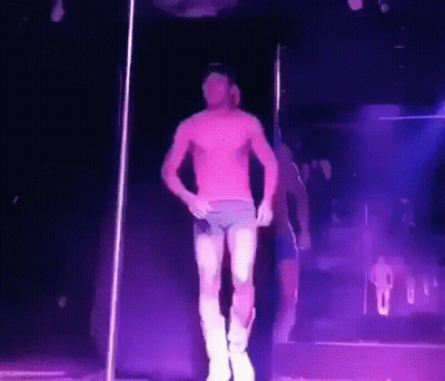 A Man Without A Shirt Is Dancing On A Pole In A Dark Room GIF