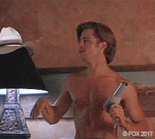 A Man Without A Shirt Is Holding A Gun In Front Of A Lamp .. GIF