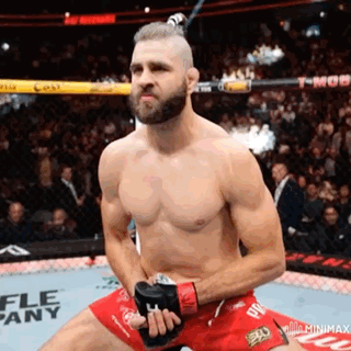 A Man Without A Shirt Is Kneeling Down In A Boxing Ring Holding A Pair Of Gloves . GIF