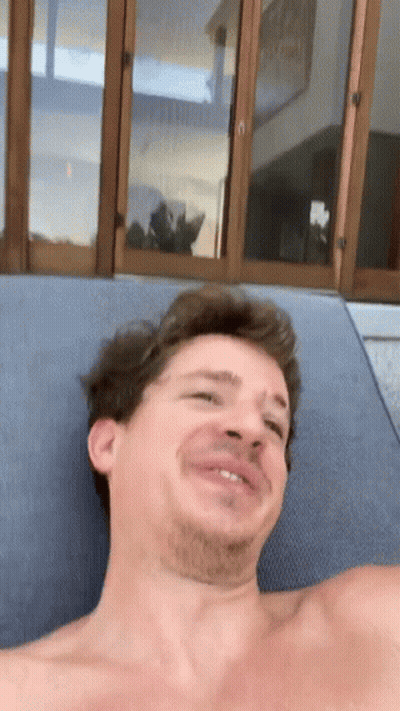 A Man Without A Shirt Is Laying On A Lounge Chair Making A Funny Face GIF