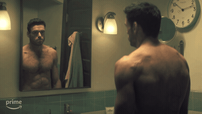 A Man Without A Shirt Is Looking At Himself In A Bathroom Mirror With A Clock On The Wall Above Him That Says Prime GIF
