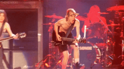A Man Without A Shirt Is Playing A Guitar On Stage In Front Of A Drum Set . GIF