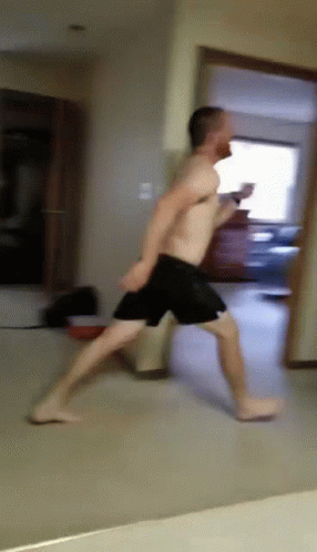 A Man Without A Shirt Is Running Through A Hallway GIF