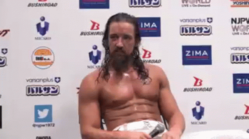 A Man Without A Shirt Is Sitting In Front Of A Wall With Logos On It GIF