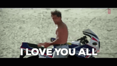 A Man Without A Shirt Is Sitting On A Motorcycle On The Beach And Saying I Love You All . GIF