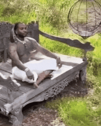 A Man Without A Shirt Is Sitting On A Wooden Bench In The Woods . GIF