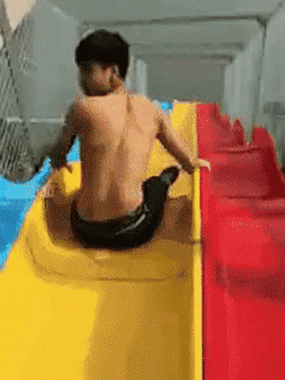 A Man Without A Shirt Is Sitting On A Yellow And Red Slide GIF
