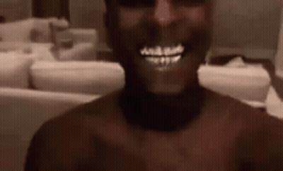 A Man Without A Shirt Is Smiling In A Living Room . GIF