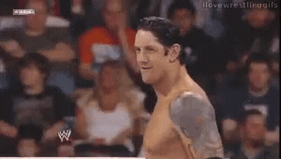 A Man Without A Shirt Is Smiling In Front Of A Crowd Of People . GIF