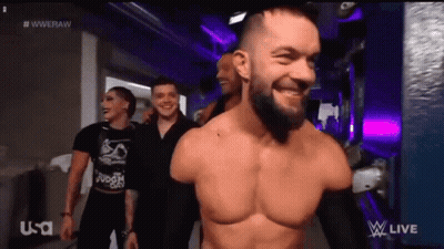 A Man Without A Shirt Is Smiling While Walking Down A Hallway With Other People . GIF
