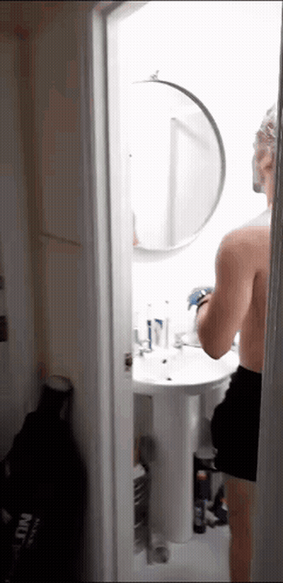 A Man Without A Shirt Is Standing In A Bathroom Looking At Himself In A Mirror GIF
