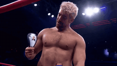 A Man Without A Shirt Is Standing In A Boxing Ring Holding A Trophy . GIF
