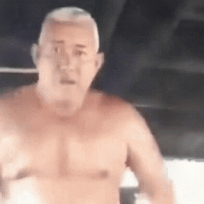 A Man Without A Shirt Is Standing In A Dark Room And Looking At The Camera . GIF