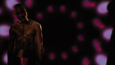 A Man Without A Shirt Is Standing In A Dark Room With Purple Lights Behind Him GIF
