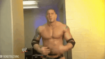 A Man Without A Shirt Is Standing In A Hallway With A Wrestling Logo On The Wall Behind Him . GIF