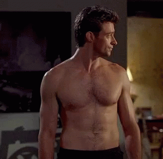 A Man Without A Shirt Is Standing In A Room . GIF