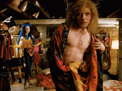 A Man Without A Shirt Is Standing In A Room Surrounded By People GIF
