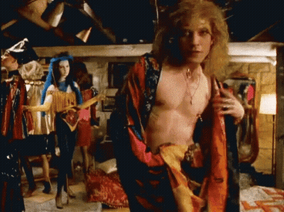 A Man Without A Shirt Is Standing In A Room With Clothes On Display . GIF