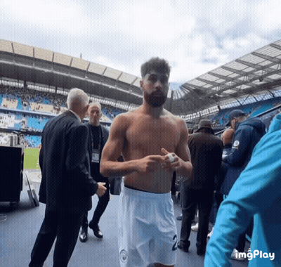 A Man Without A Shirt Is Standing In A Stadium With A Man In A Suit Standing Behind Him GIF