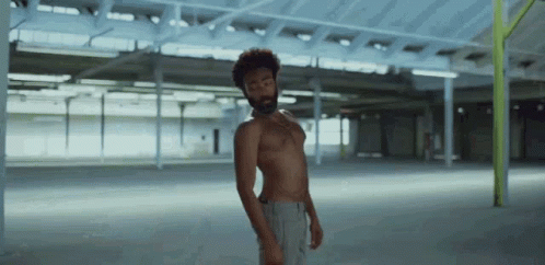 A Man Without A Shirt Is Standing In An Empty Room . GIF