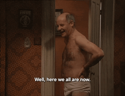 A Man Without A Shirt Is Standing In Front Of A Bed With The Words Well Here We All Are Now All The Lads GIF
