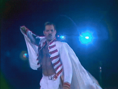 A Man Without A Shirt Is Standing In Front Of A Blue Light And Holding A Microphone GIF