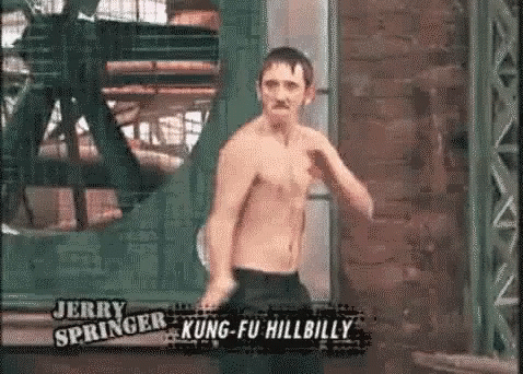 A Man Without A Shirt Is Standing In Front Of A Brick Wall In A Room . GIF